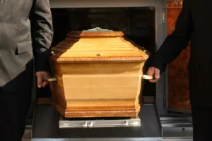 Deux porteurs en costume tenant les poignées d'un cercueil en bois traditionnel.
