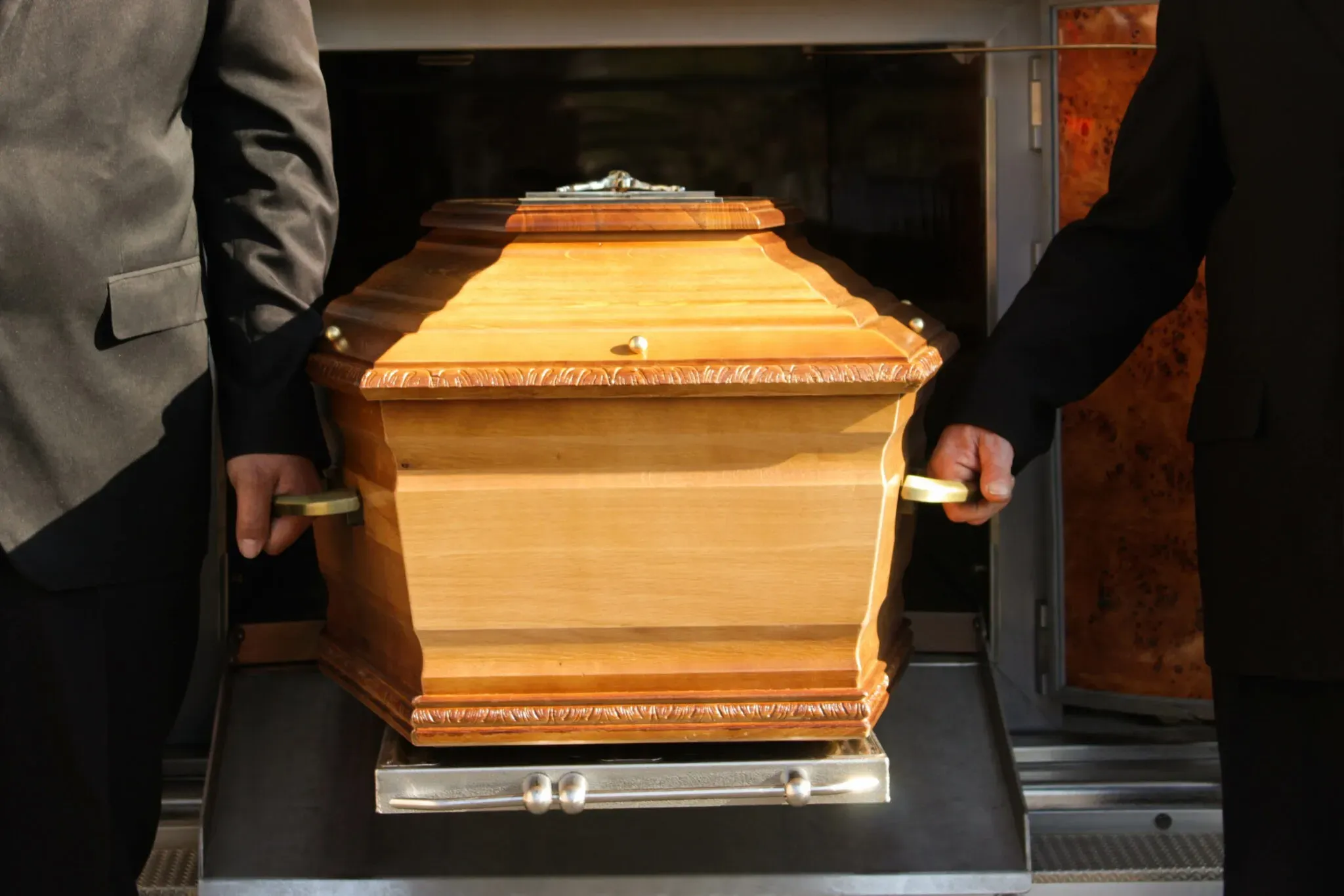 Deux porteurs en costume tenant les poignées d'un cercueil en bois traditionnel.