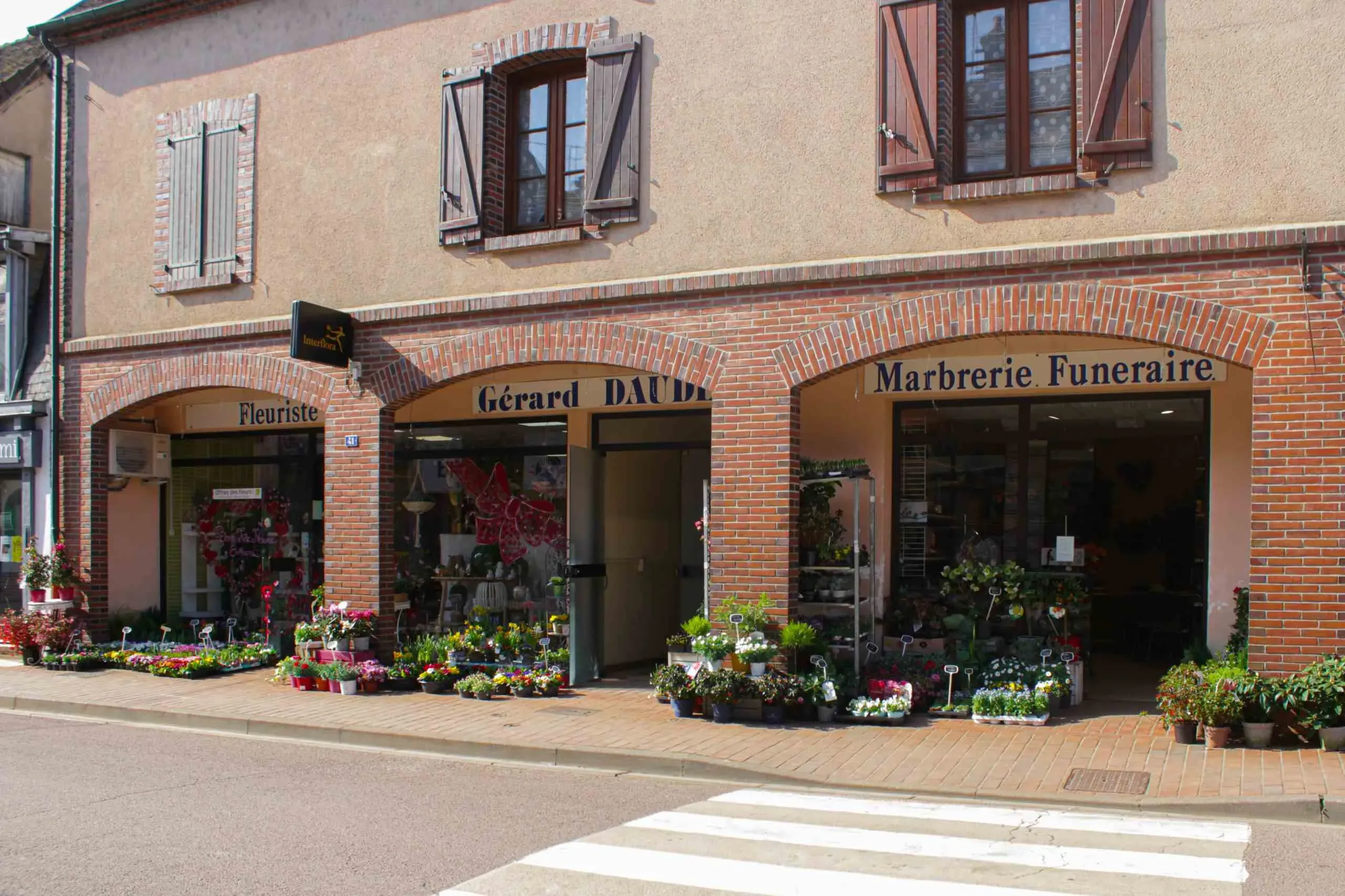 Façade en briques d'une marbrerie funéraire et fleuriste avec plantes en devanture.